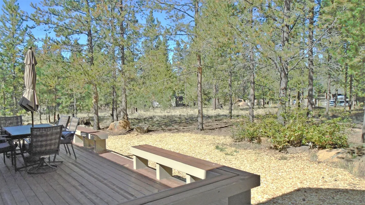 A peaceful patio seating area surrounded by trees, featuring a large wooden bench and space for outdoor dining or relaxing. The natural setting emphasizes the connection between the home and the outdoors, perfect for family meals or post-adventure relaxation.