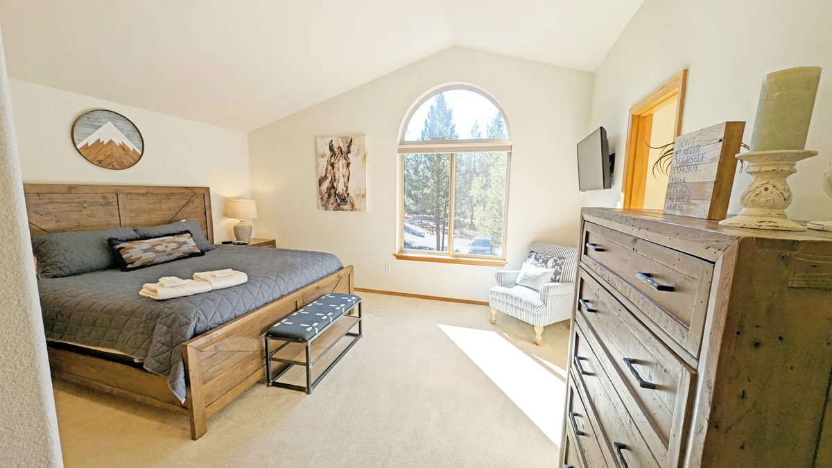 A tranquil bedroom featuring a comfortable bed dressed in plush linens, a window framing natural light, an inviting armchair, and a wooden dresser. The ambiance is serene and restful, ideal for relaxation and unwinding after a long day.