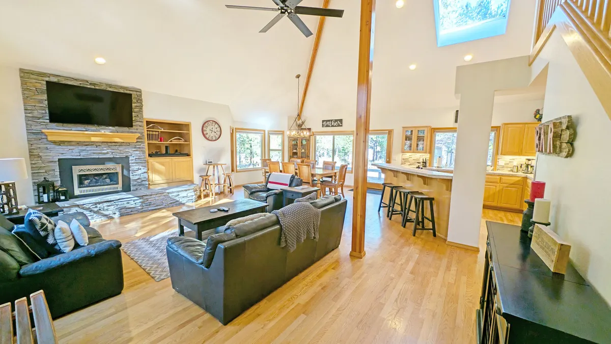 A spacious and light-filled open-plan living area featuring a cozy fireplace, large windows that flood the space with sunlight, a modern kitchen island perfect for casual breakfasts, a welcoming dining area, and comfortable sofas arranged for easy socializing.