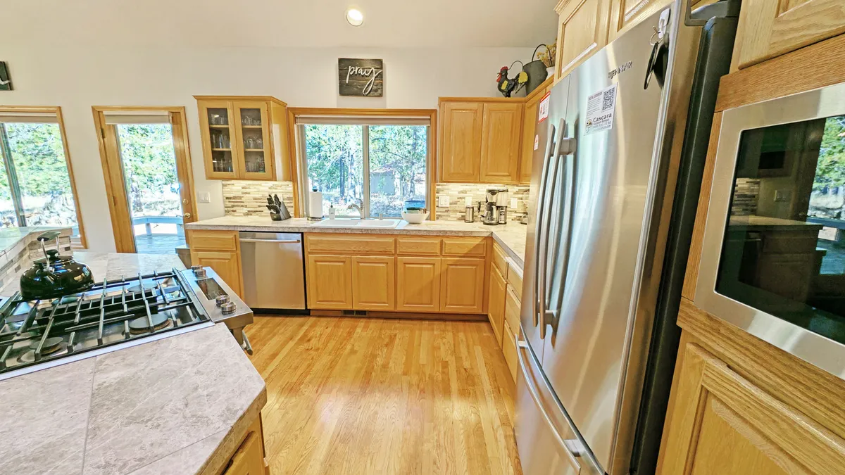 A bright, inviting kitchen with stainless steel appliances, a central island ideal for meal prep or casual dining, wood cabinetry, and expansive windows offering a view and ample daylight.