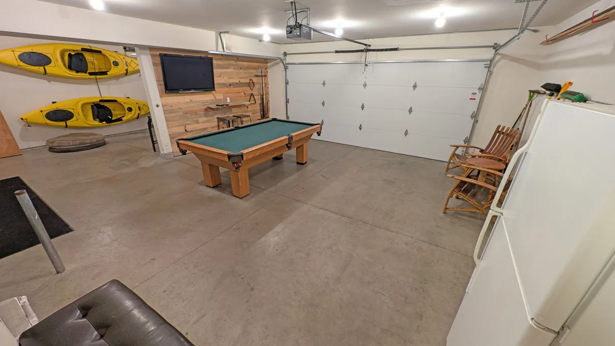 A vibrant, recreational interior space featuring a pool table, kayaks, a television, refrigerator, and rocking chairs. The area feels casual and fun, inviting families or groups to unwind together with games or movies after a day of outdoor activities.